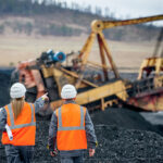 Mining employees at a site with rusted equipment in the background, showing the impact of corrosion on mining equipment.